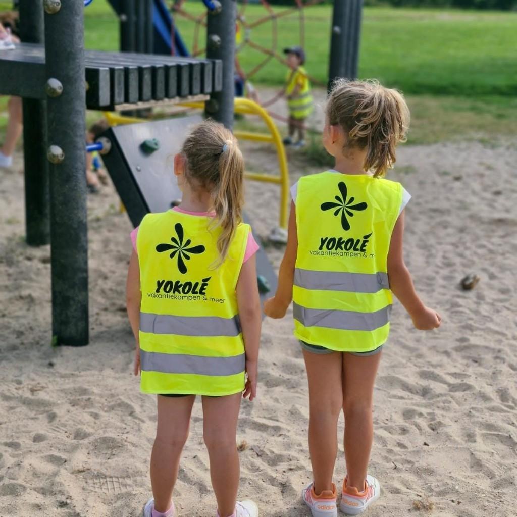 Twee meisjes in gele Yokolé-hesjes op de speelplaats